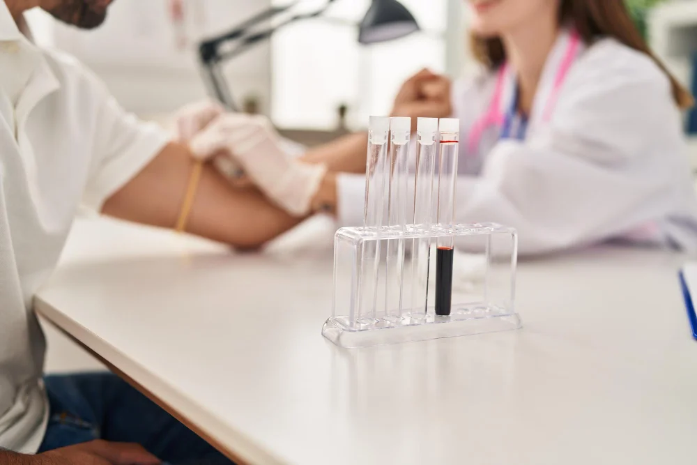 Patient undergoing blood collection with test tubes displayed on a table during a health screening in Livonia, MI.